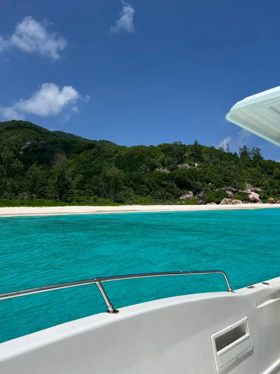 Tropical blue waters and palm-lined green shores of Anse Coco Beach in Seychelles, seen from a boat.
